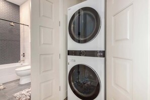 A laundry room with two front-loading washing machines, a white door, and a bathroom with a bathtub and toilet visible through an open door. - NEW|Palo Verde Suite @ Cedara| Penthouse|Old Town (Scottsdale)
