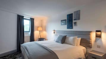 A hotel room with a large bed, a bedside table, a lamp, and a window with curtains.