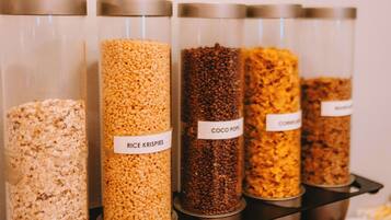 Cuatro frascos de vidrio con tapas metálicas, cada uno etiquetado con un tipo diferente de cereal: Rice Krispies, Coco Pops, Corn Flakes y otro cereal.