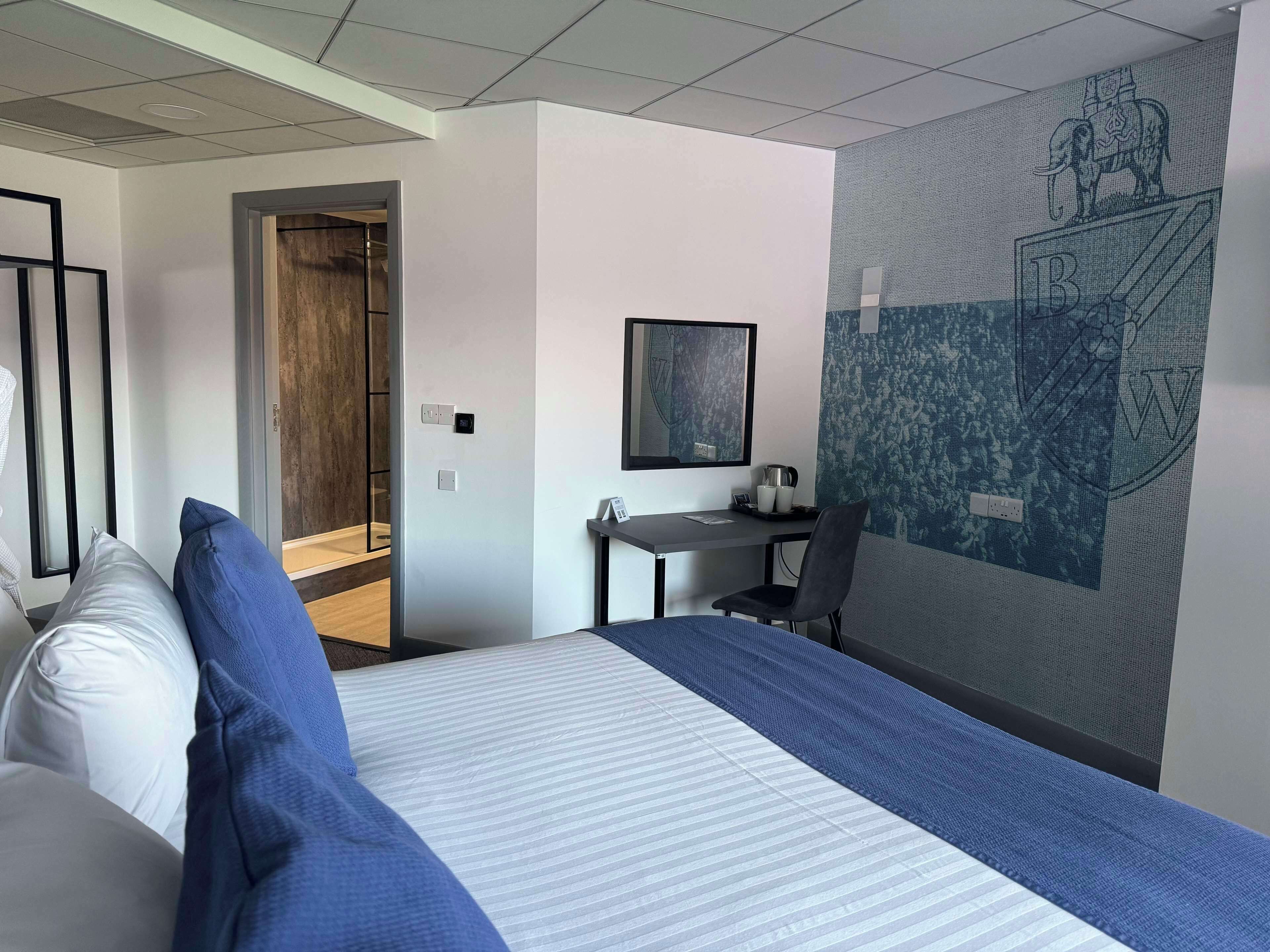 A hotel room with a bed, a desk, a chair, and a large wall mural.