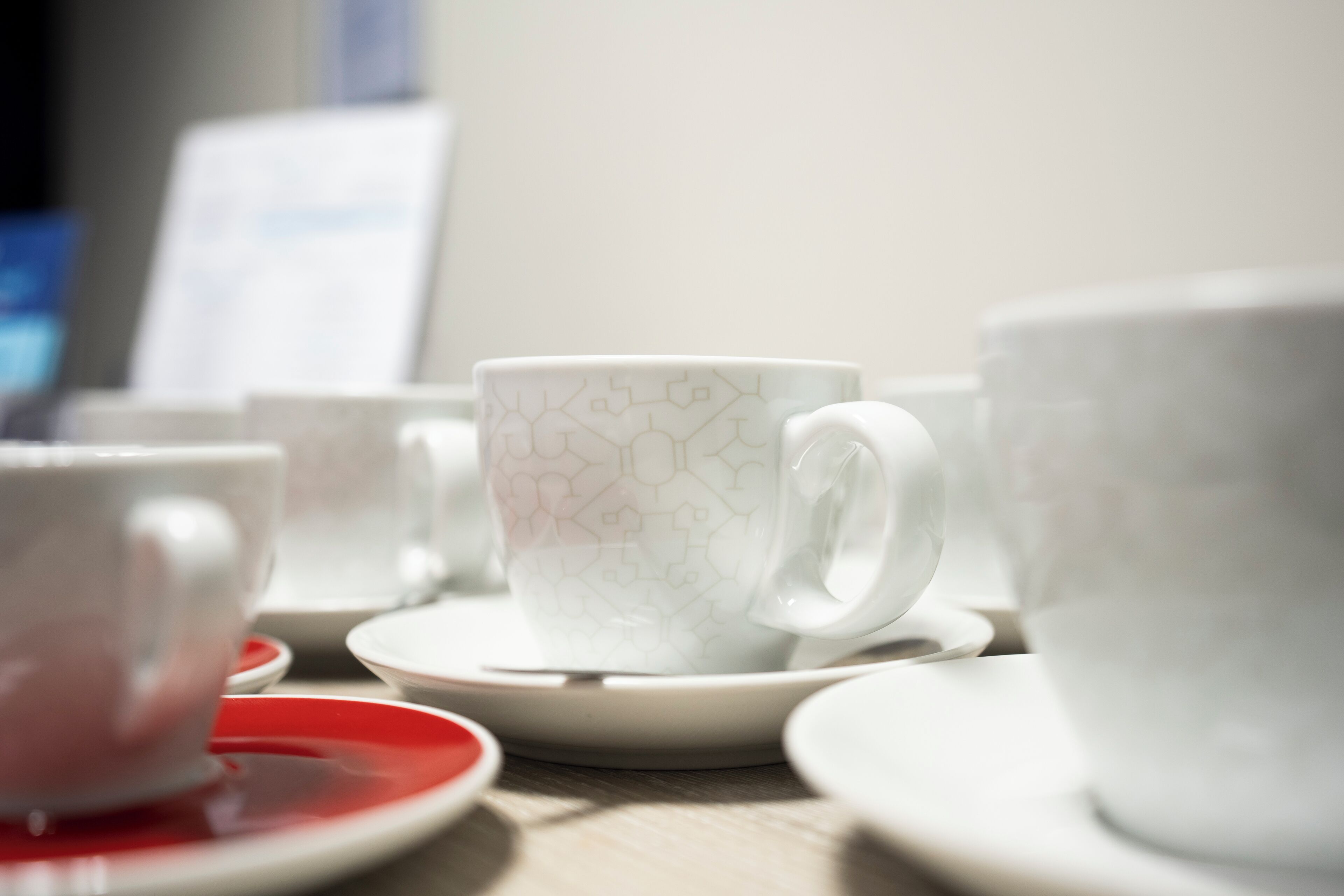 A close-up of a white ceramic cup with a geometric pattern on a saucer, part of a tea set.