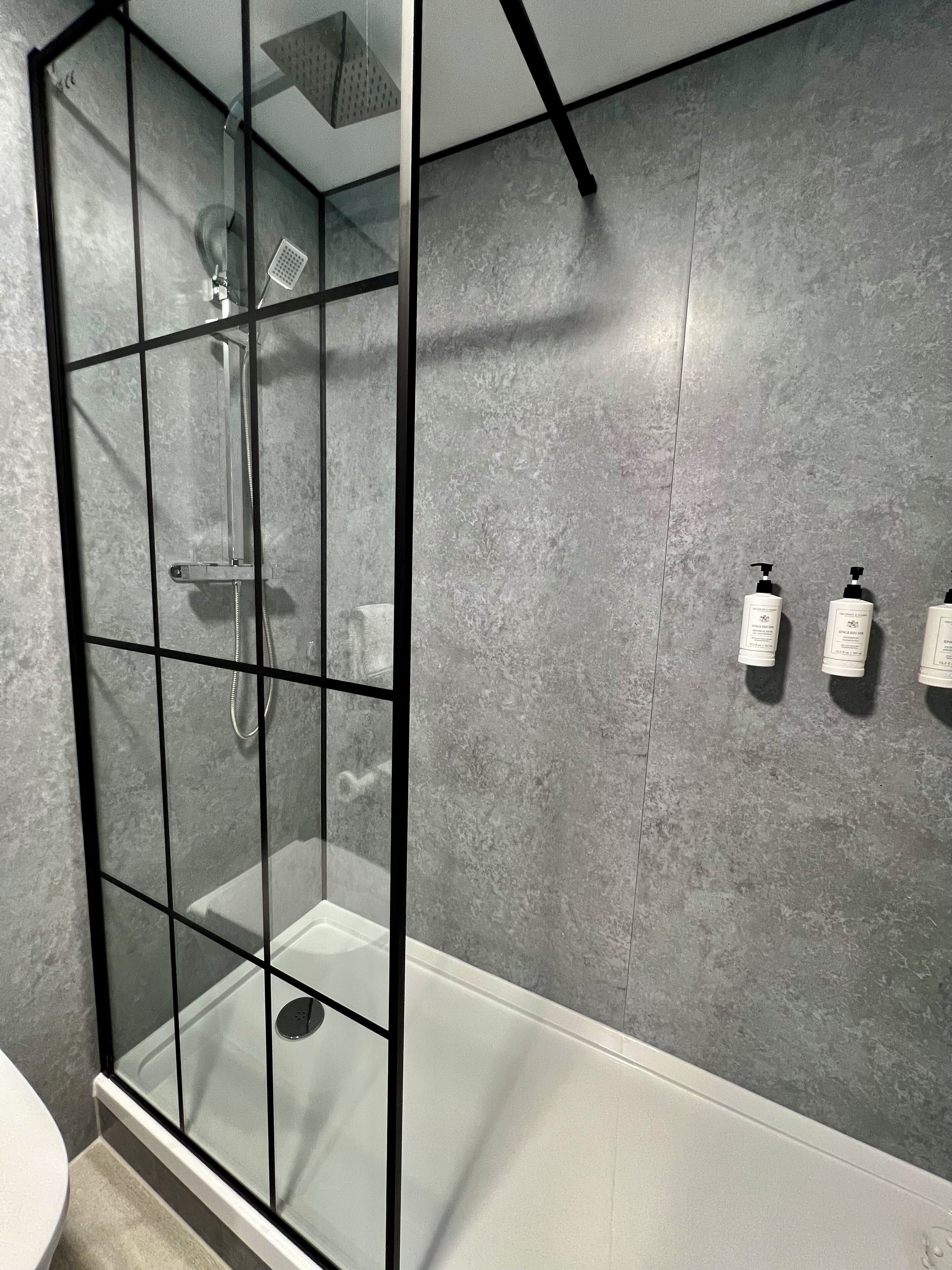 Une salle de bain moderne avec une douche à parois de verre, une baignoire blanche et un mur gris à texture.