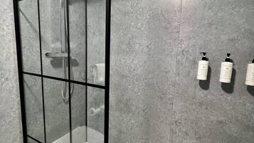 Un baño moderno con ducha de vidrio, bañera blanca y pared gris con textura.