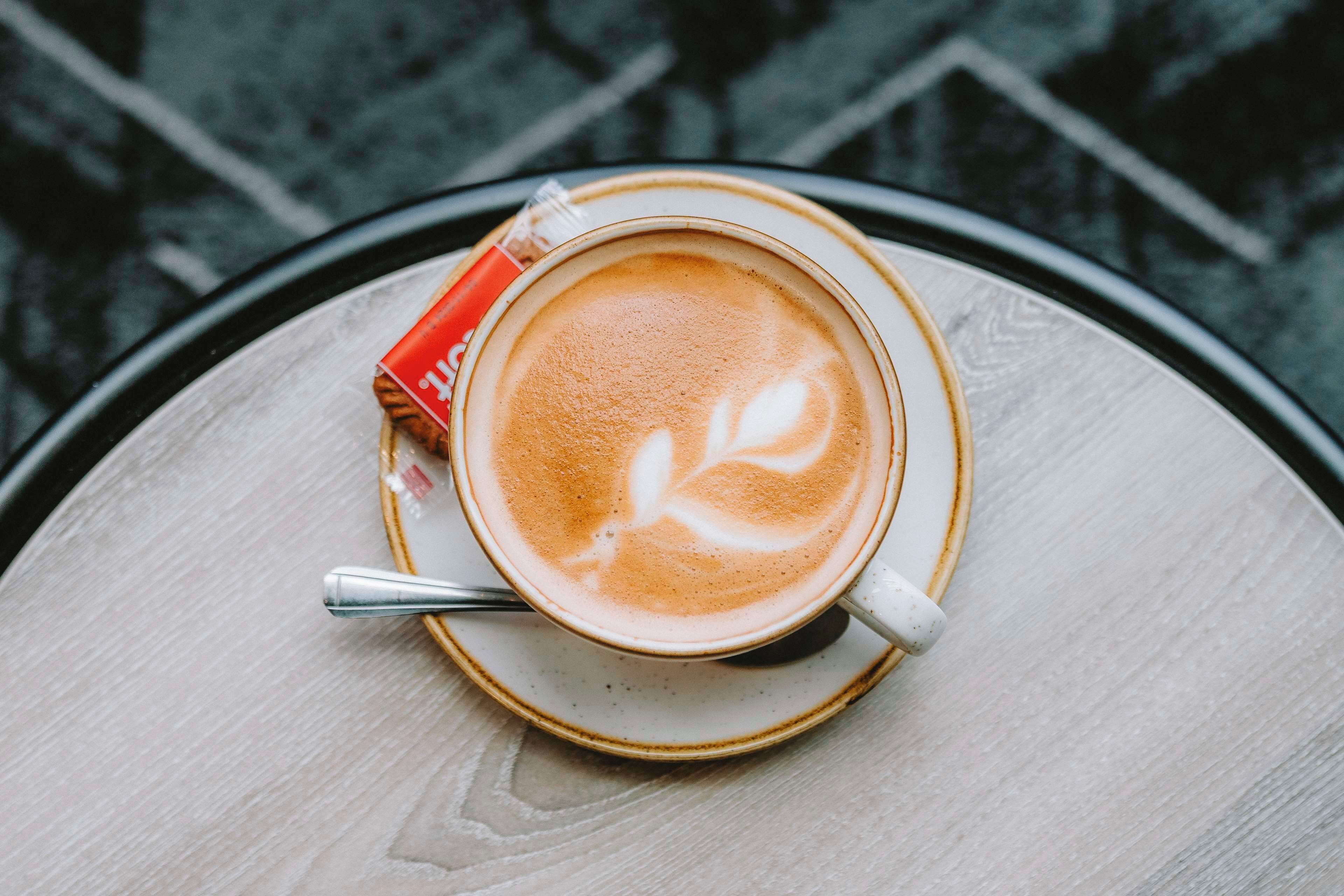 Een kop koffie met latte-art op een schotel, geplaatst op een ronde tafel.
