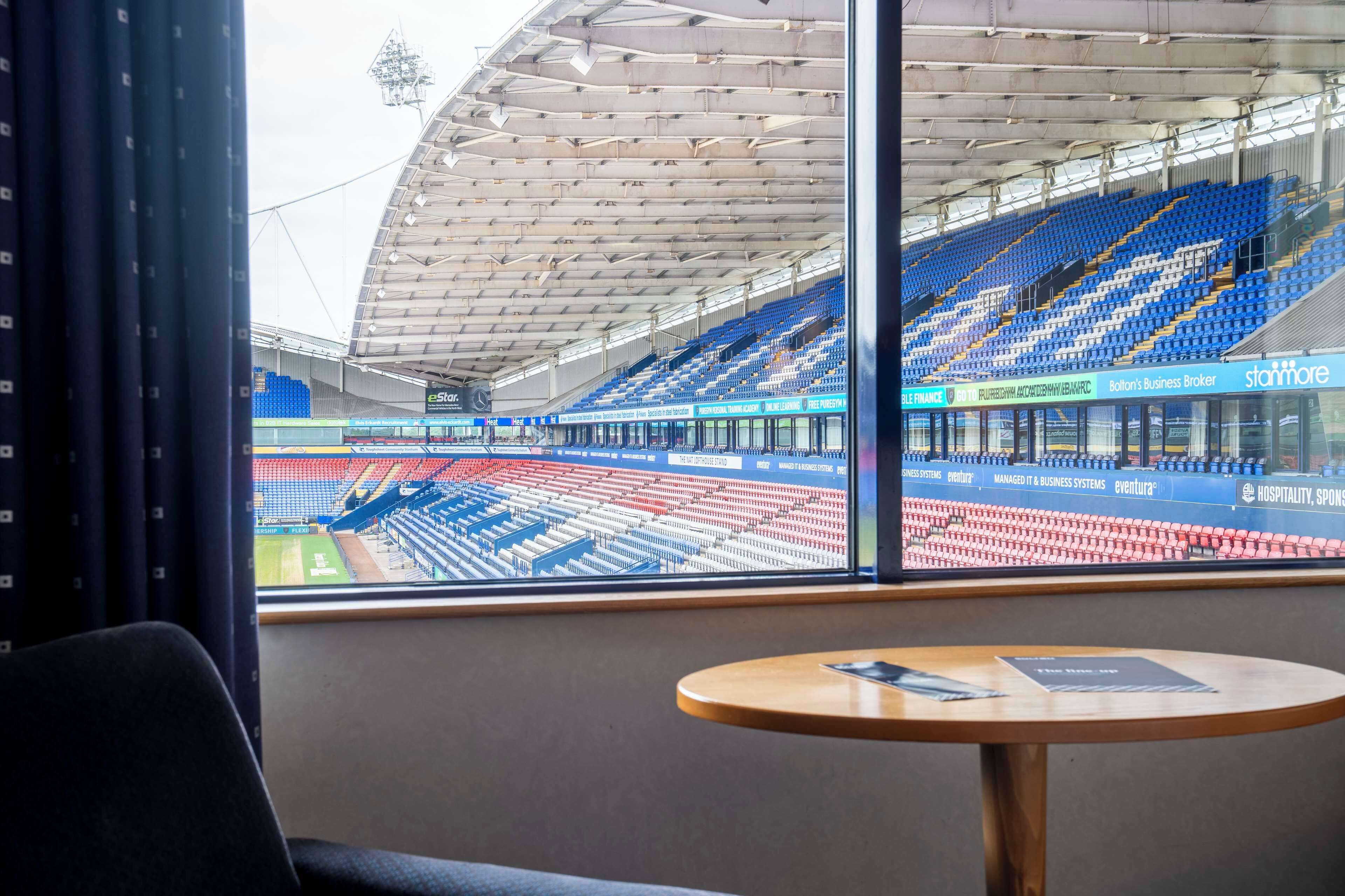 A stadium with empty blue and red seats, a large open space, and a table with a menu.