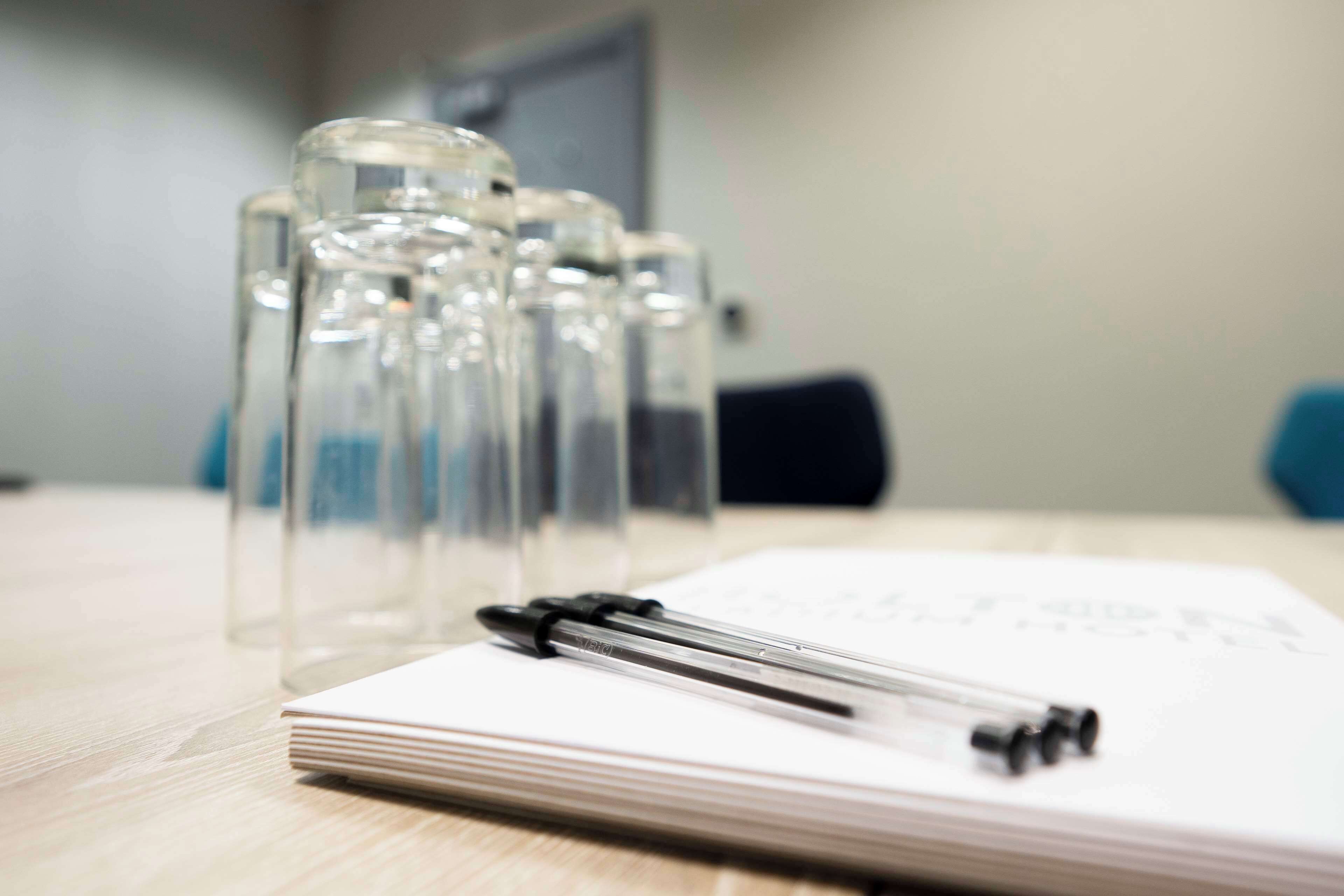 Un carnet et un stylo posés sur une table en bois, accompagnés de plusieurs bouteilles en verre transparent.