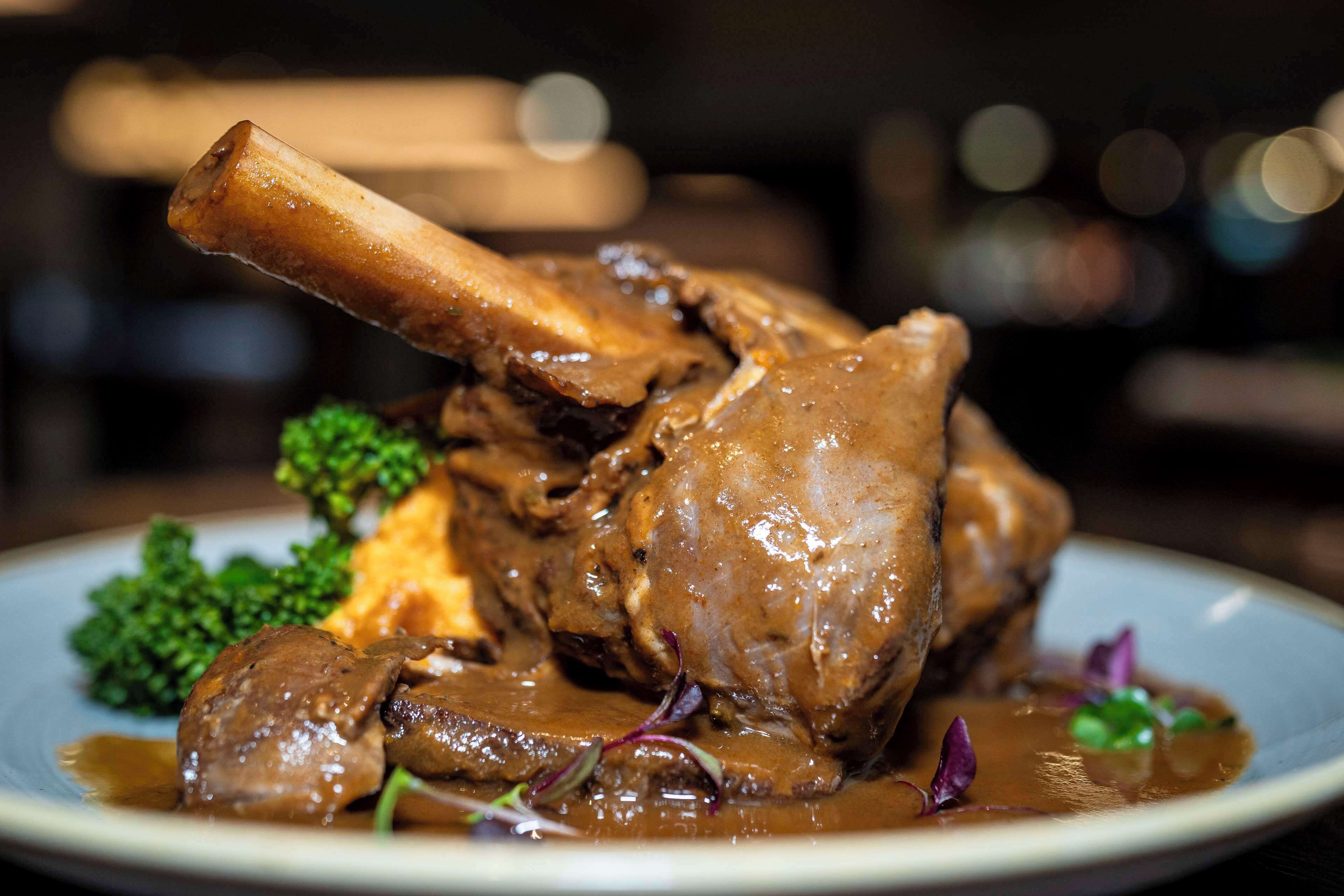 A plate of food with a large piece of meat, possibly a steak, accompanied by a side of greens and a sauce.