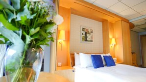 A hotel room with a bed, two bedside lamps, a nightstand, and a floral arrangement. - The Bolton Stadium Hotel, a member of Radisson Individuals (Bolton)