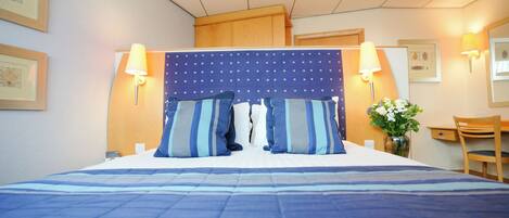 Una habitación de hotel con una cama grande, dos lámparas de noche, un cabecero de madera, un escritorio con una silla y un jarrón con flores.