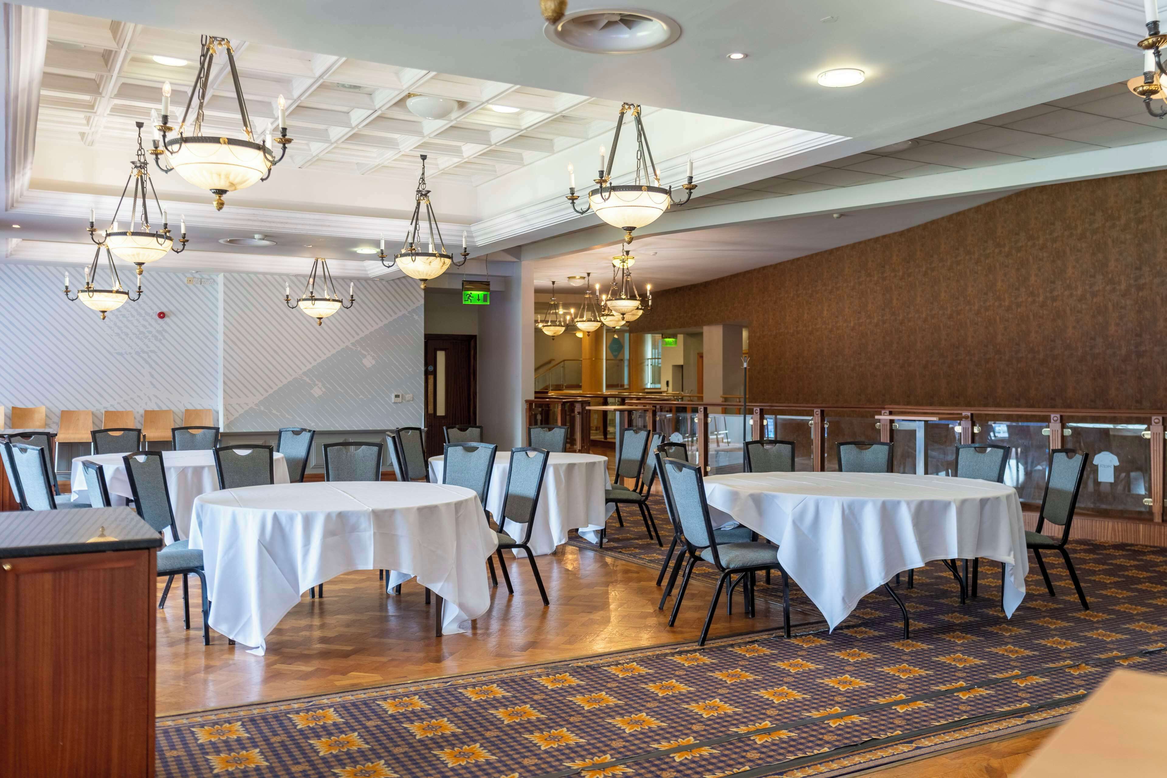 A banquet hall with round tables covered in white tablecloths, arranged in rows.