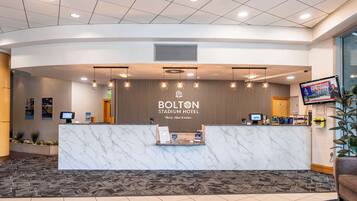 A reception area with a marble counter, digital screens, and a sign for the Bolton Stadium Hotel.