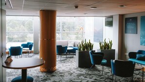 A modern lounge area with a large pillar, blue chairs, a sofa, and a coffee table. - The Bolton Stadium Hotel, a member of Radisson Individuals (Bolton)