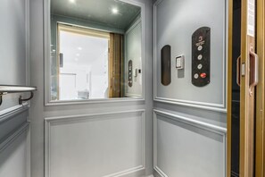 A modern elevator with a control panel, a mirror, and a window with a view of the outside.