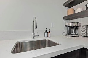 Eine Küche mit einem Edelstahlspülbecken, einem modernen Wasserhahn, einer Kaffeemaschine und zwei Handseifenflaschen auf der Arbeitsplatte.