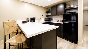 Une cuisine moderne dotée d’un îlot central, de meubles de rangement aux couleurs sombres et d’un réfrigérateur noir.