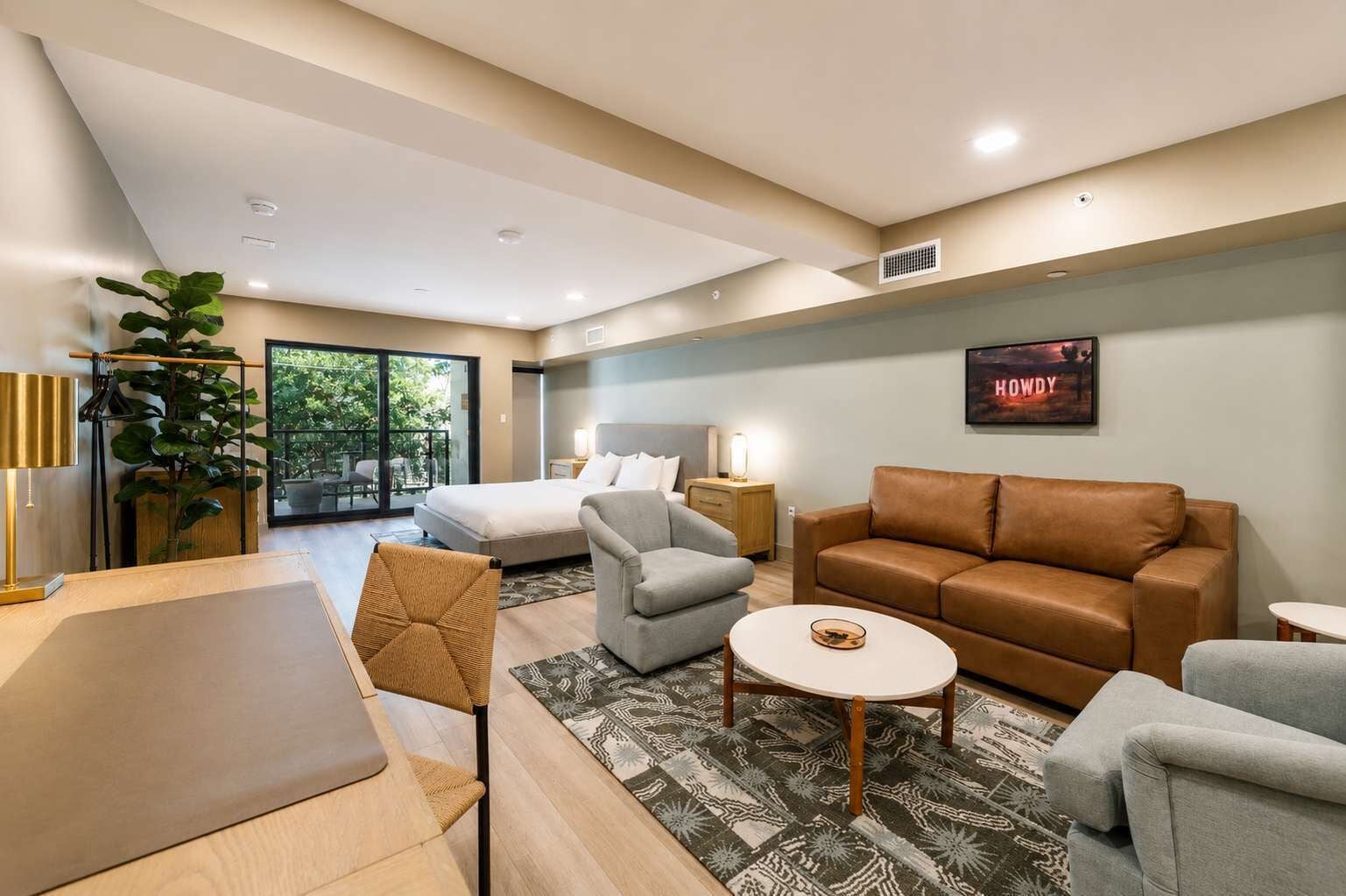 A modern hotel room with a bed, sofa, armchair, and a dining area.