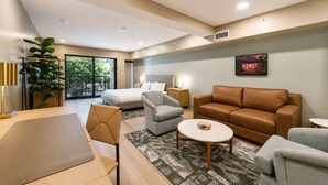 Una habitación de hotel moderna con cama, sofá, sillón y zona de comedor.