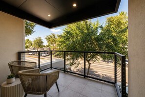 A balcony with two wicker chairs, a small potted plant, and a view of a street with trees and parked cars. - NEW|Luxe Ocotillo Suite @ Cedara|Heart of Old Town (Scottsdale)