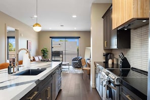 A modern kitchen with a large island, built-in appliances, and a view to an outdoor balcony.