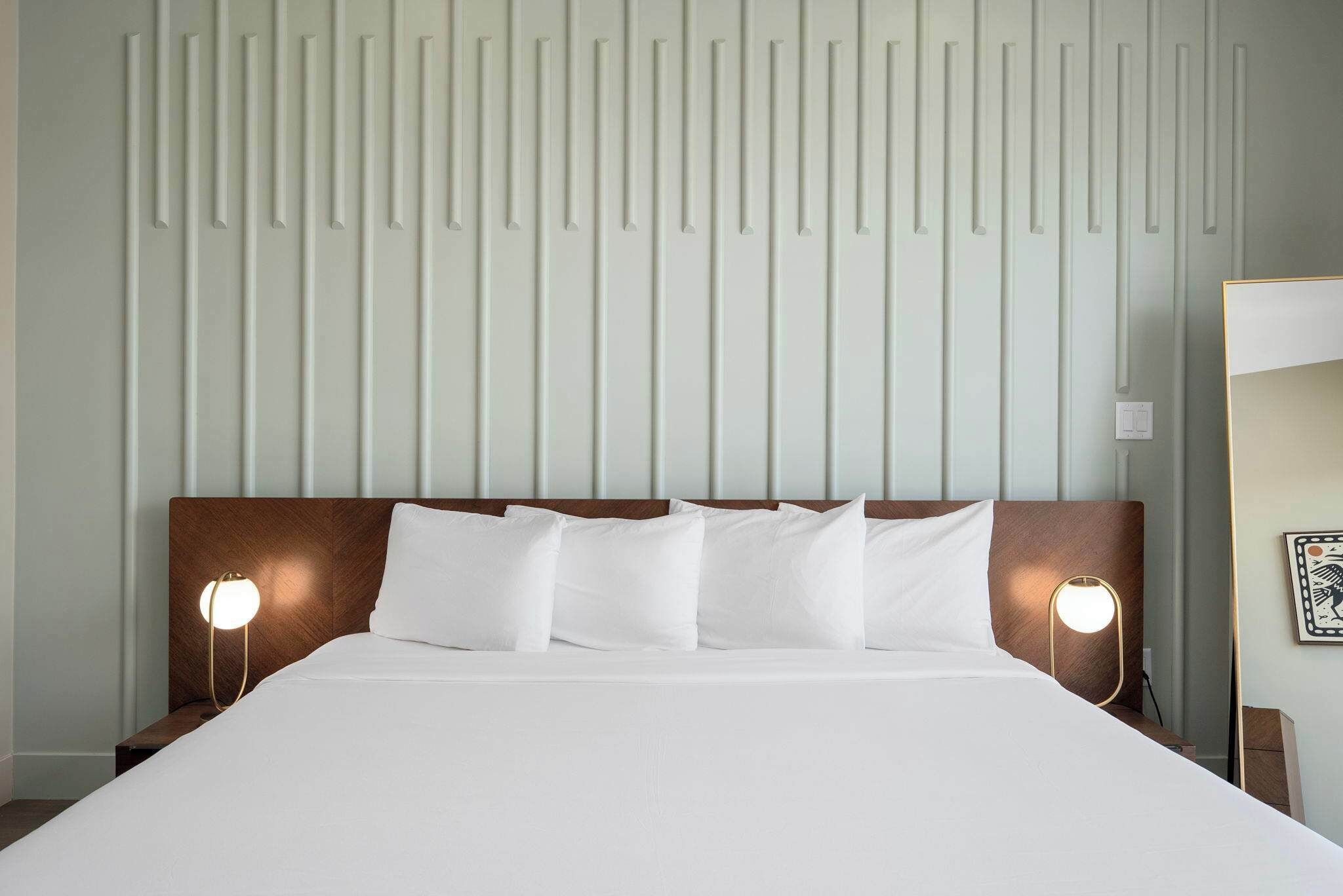 Una habitación de hotel con una cama grande, dos lámparas de noche y una pared con paneles verticales.