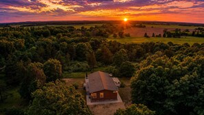 Una casa rodeada de un bosque frondoso con un atardecer de fondo.