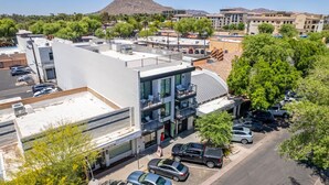 A modern building with a flat roof, multiple balconies, and a parking lot with cars. - NEW|Luxe Cypress Suite @ Cedara |Heart of Old Town (Scottsdale)