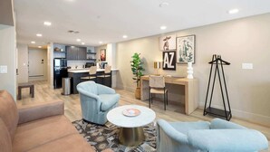 A modern living room with a sofa, two armchairs, a coffee table, and a desk with a chair. There is a kitchen area in the background with cabinets and a refrigerator. - NEW|Luxe Cypress Suite @ Cedara |Heart of Old Town (Scottsdale)