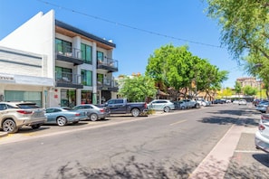 Vista callejera con coches aparcados, un edificio con balcones y árboles.