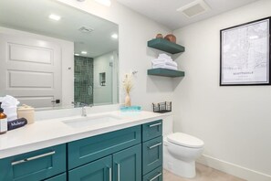 Une salle de bain moderne avec un lavabo blanc, des meubles de couleur turquoise, des toilettes blanches et un grand miroir.