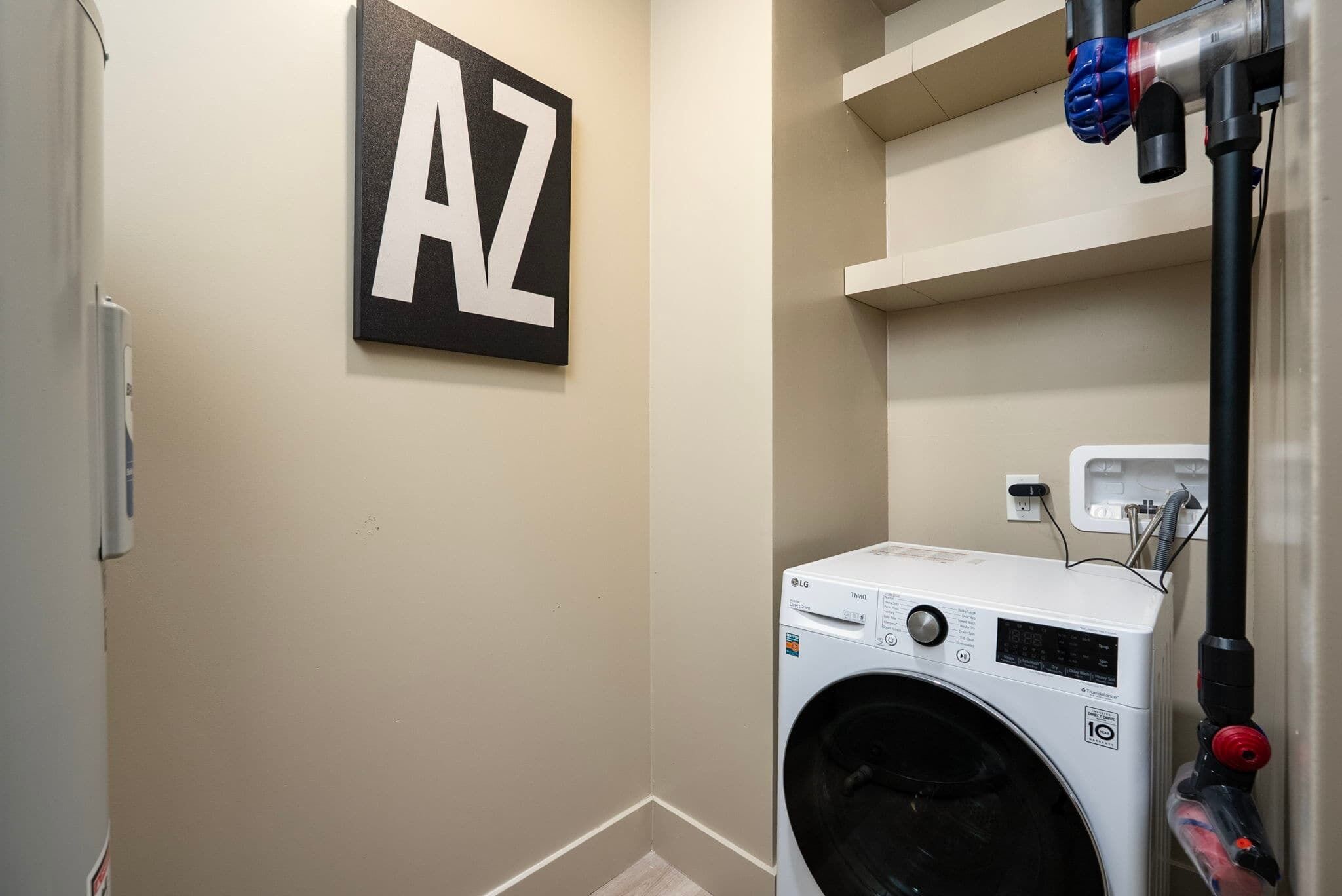 A laundry room with a washing machine, a wall-mounted heater, and a shelf with a letter 'AZ' sign.
