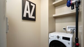 Un lavadero con lavadora, un calentador de pared y un estante con un letrero con la letra 'AZ'.