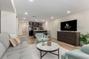 Un salon moderne comprenant un canapé, un fauteuil, une table basse et un téléviseur à écran plat.