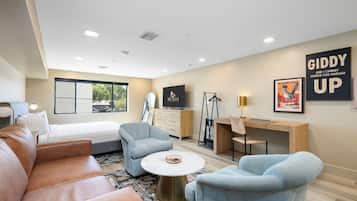 A modern hotel room with a bed, a desk, a chair, a sofa, and a television.