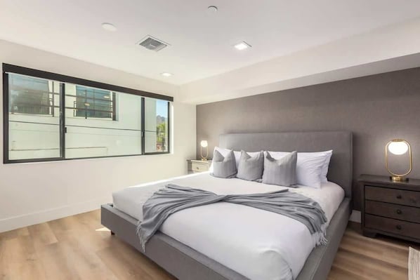 Une chambre moderne avec un grand lit, une table de chevet, une petite table de nuit avec une lampe et une grande fenêtre.