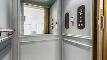 A modern elevator with a control panel, a mirror, and a window with a view of the outside.