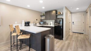 Una cocina moderna con una isla central, taburetes de bar, una cafetera, un microondas, un tostador y un refrigerador.