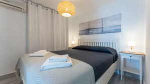 Et moderne hotelværelse med en pænt redt seng, et natbord med lampe, en fastgjort aircondition og et stort abstrakt maleri.
