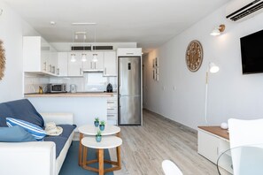 Une cuisine moderne avec des meubles blancs, un réfrigérateur en acier inoxydable et un coin repas comprenant une table blanche et des coussins bleus.