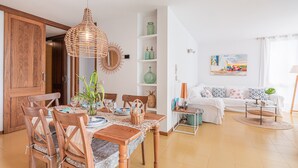 A dining area with a wooden table and chairs, a hanging light fixture, and a white sofa in the background. - "Apartamento Mirella" with Pool, Balcony, and Wi-Fi (port de pollença)