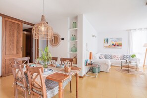 A dining area with a wooden table and chairs, a hanging light fixture, and a white sofa in the background.