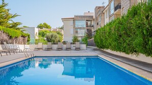 A swimming pool with lounge chairs, surrounded by greenery and modern buildings. - "Apartamento Mirella" with Pool, Balcony, and Wi-Fi (port de pollença)