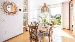 A dining area with a table set for four, wooden chairs, a woven pendant light, and a view of the outdoors. - "Apartamento Mirella" with Pool, Balcony, and Wi-Fi (port de pollença)