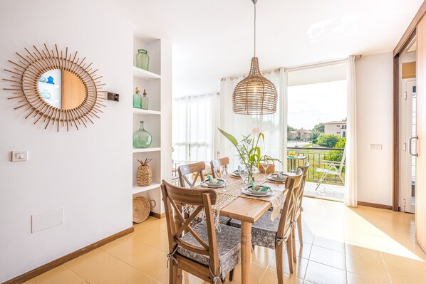 A dining area with a table set for four, wooden chairs, a woven pendant light, and a view of the outdoors.