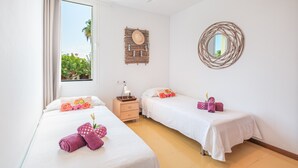 A hotel room with two beds, a ceiling fan, a bedside table with a lamp, a wall-mounted mirror, and a view of greenery outside. - "Apartamento Mirella" with Pool, Balcony, and Wi-Fi (port de pollença)