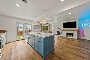 Una cocina moderna con una isla central, luces colgantes, un televisor y un letrero de neón.