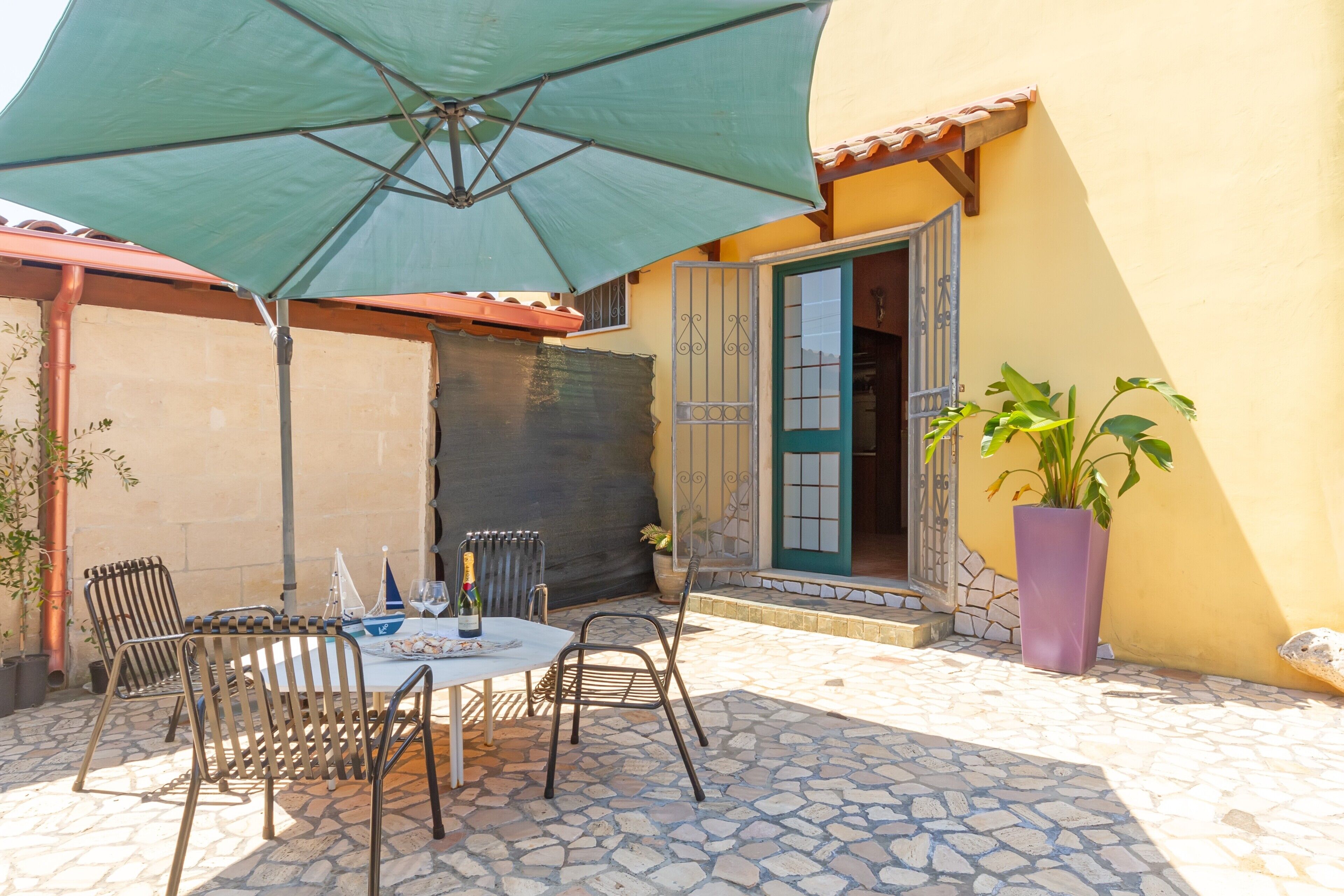 An outdoor patio with a table and chairs, a green umbrella, and a potted plant.