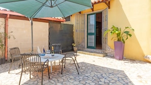 An outdoor patio with a table and chairs, a green umbrella, and a potted plant.