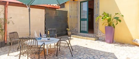 An outdoor patio with a table and chairs, a green umbrella, and a potted plant.