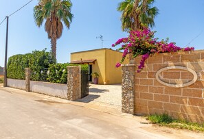 A residential property with a stone wall entrance, a yellow building, and a palm tree.