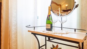 A table with a bottle of champagne, two wine glasses, and a mirror reflecting a room with a bed and a lamp.